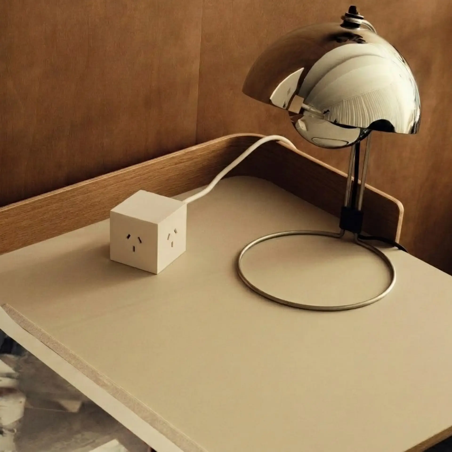 Cubo Arena sobre un escritorio beige contra una pared de madera, con una lámpara cromada