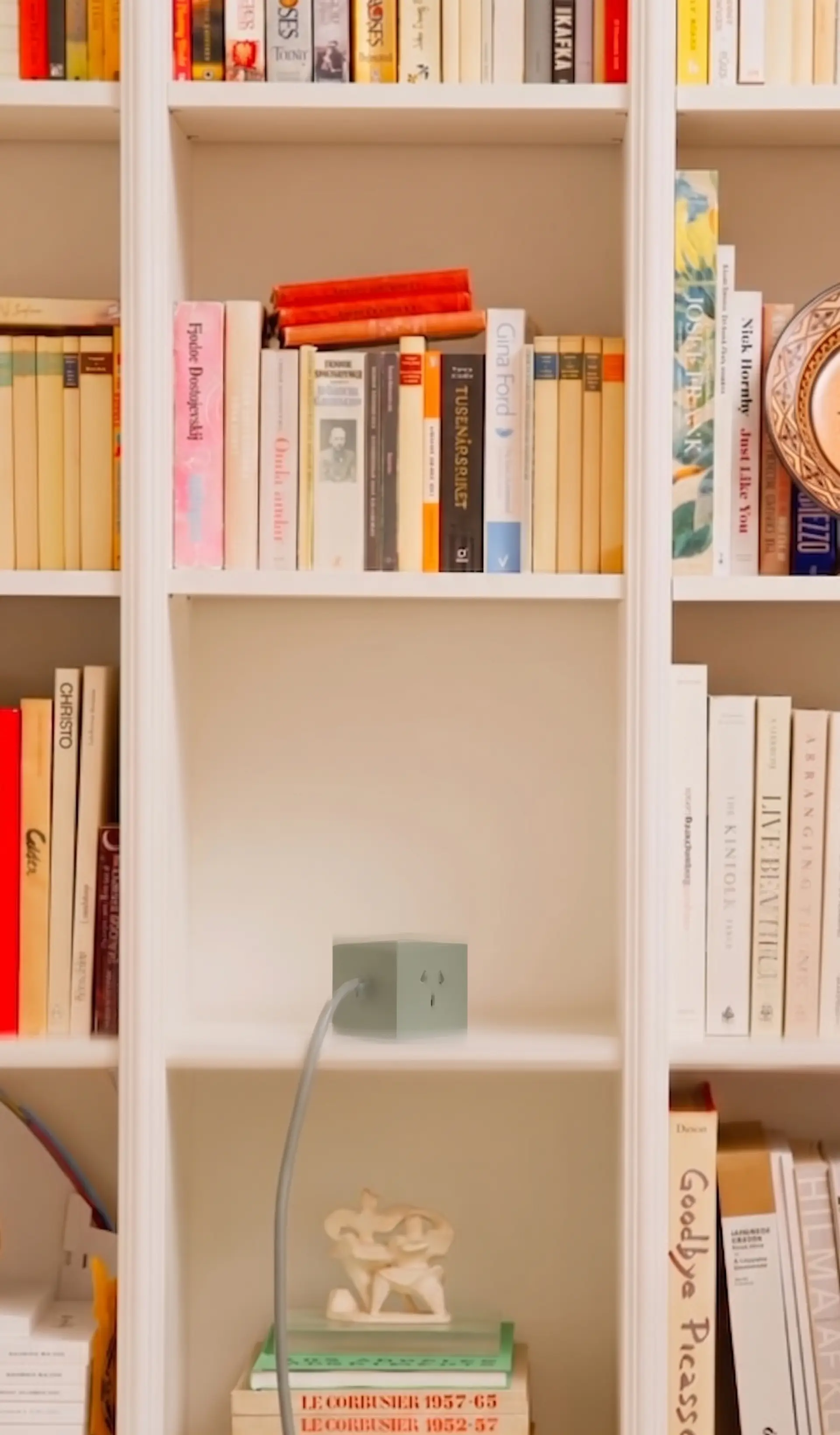 Cubo Verde en un estante vacío de una biblioteca blanca llena de libros, con el cable cayendo
