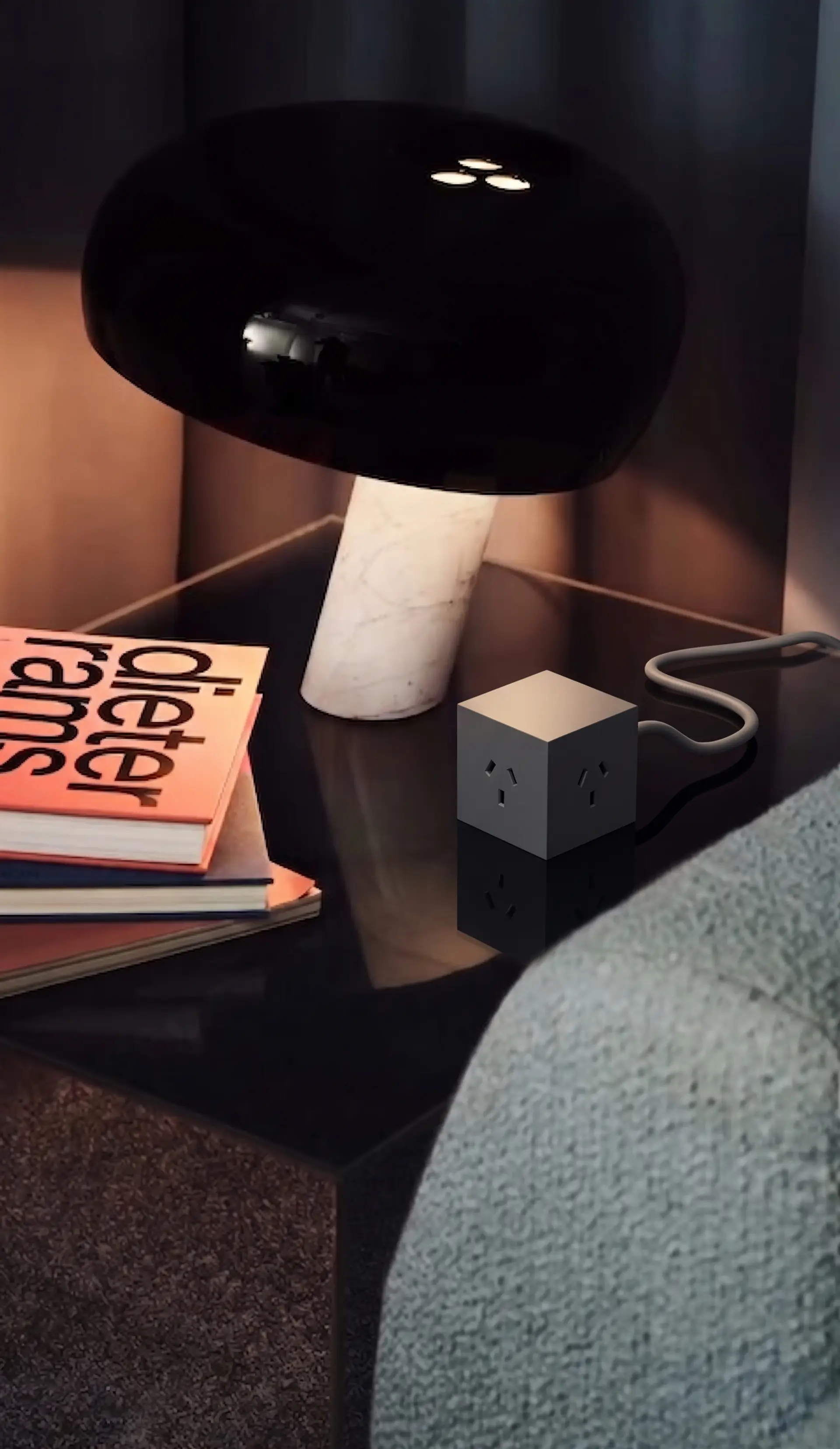 Cubo Grafito en una mesa de luz oscura junto a una lámpara y una pila de libros de diseño