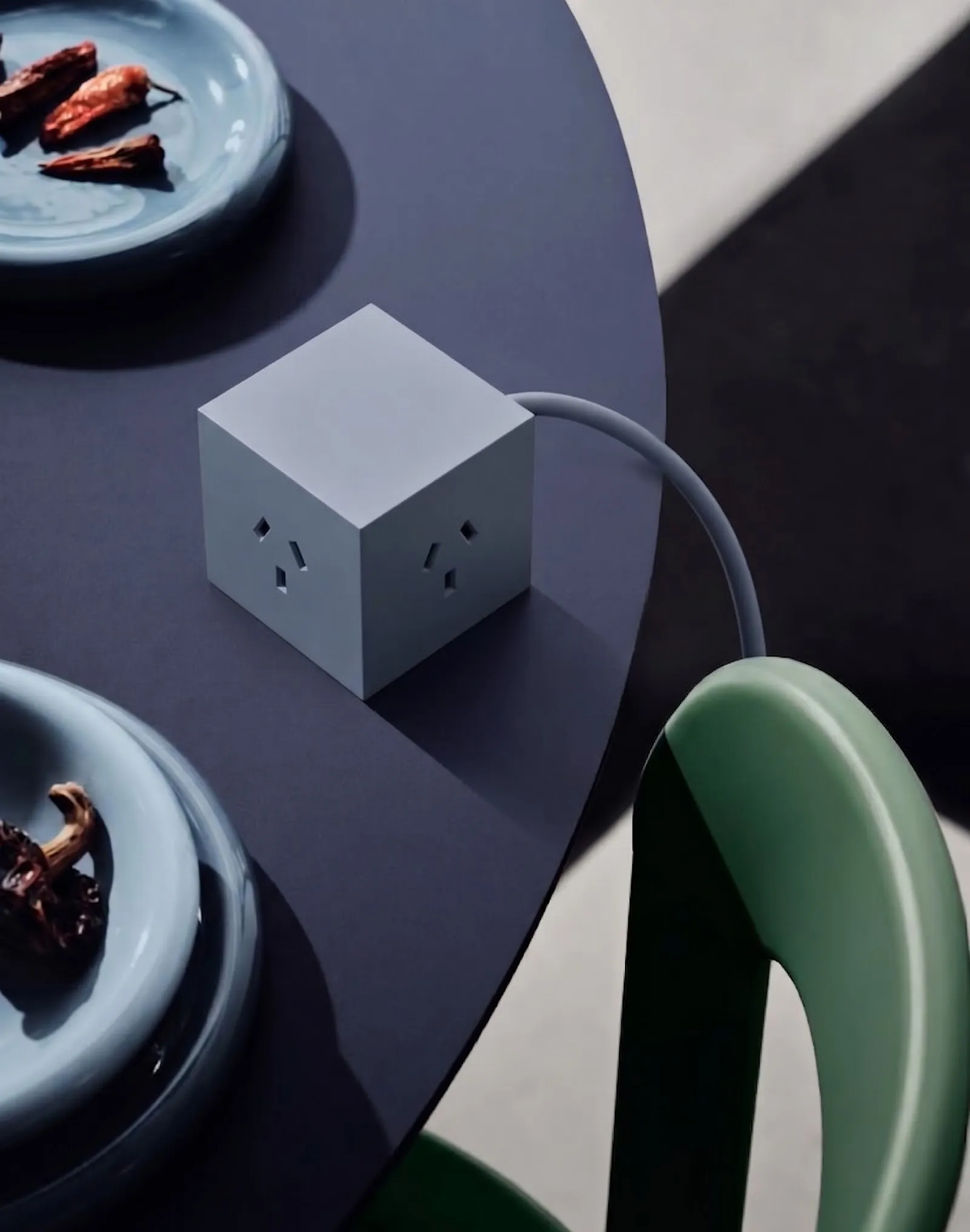 Vista cenital de una mesa violeta con dos platos celestes y el cubo Azul con el cable haciendo una curva