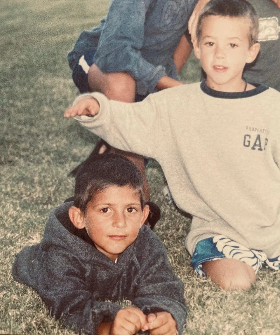 Francisco y Andrés de chicos, tirados en el pasto de una cancha, una tarde de sol